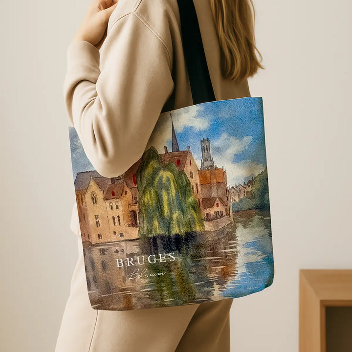 Tote bag with a scenic design of Bruges, held by a person wearing a beige coat.
