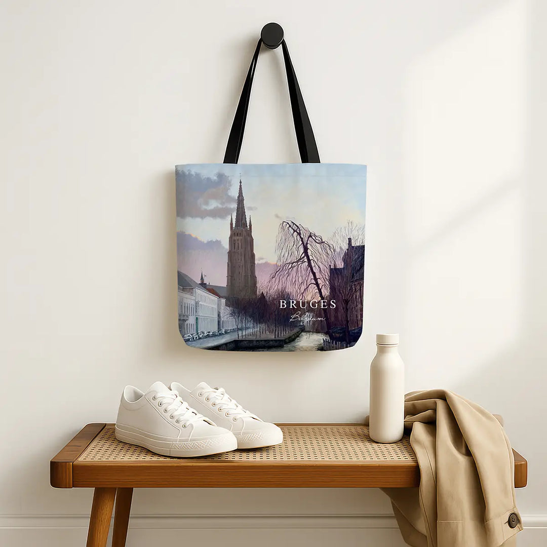 Tote bag with Bruges design hanging on a wall above a wooden bench with shoes and a bottle.