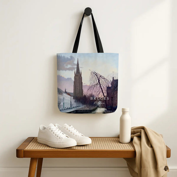 Tote bag with Bruges design hanging on a wall above a wooden bench with shoes and a bottle.