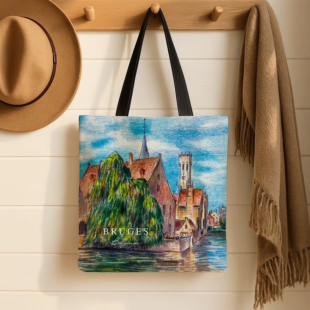 Tote bag with Bruges design hanging on a wooden hook with a hat and scarf in the background.