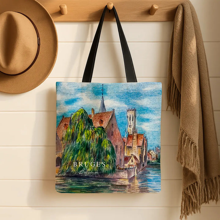 Tote bag with Bruges design hanging on a wooden hook with a hat and scarf in the background.