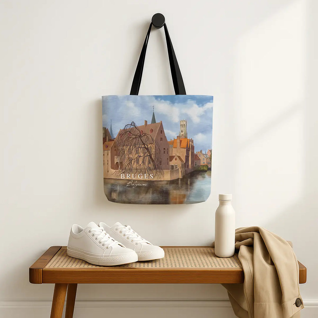 Tote bag with Bruges design hanging on a wall above a wooden bench with shoes and a bottle.