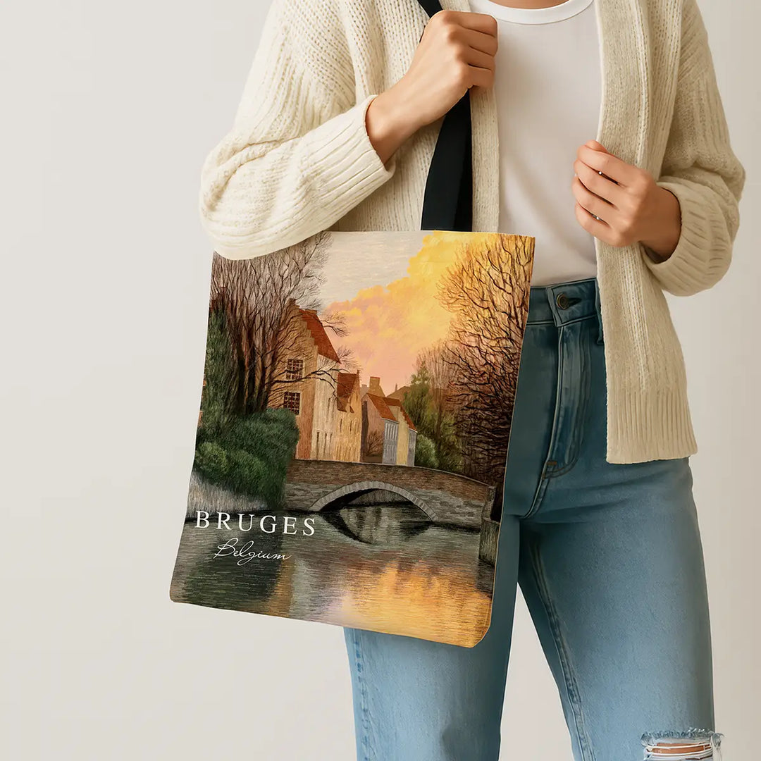 Person holding a tote bag with a scenic design and 'Bruges, Belgium' text.