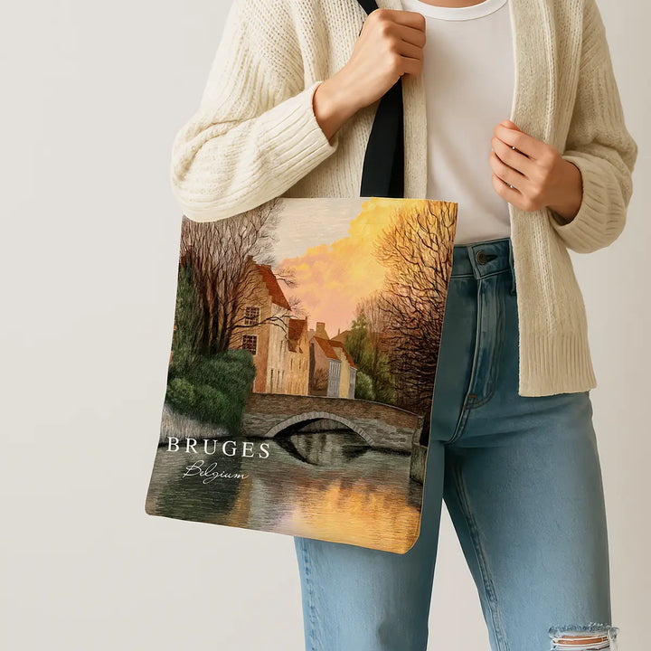 Person holding a tote bag with a scenic design and 'Bruges, Belgium' text.