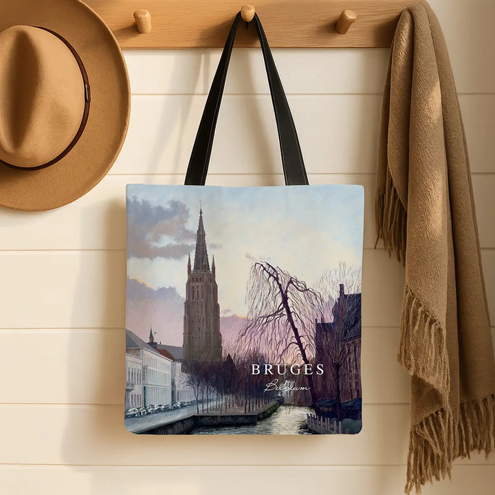 Tote bag with Bruges design hanging on a wooden hook with a hat and scarf in the background.