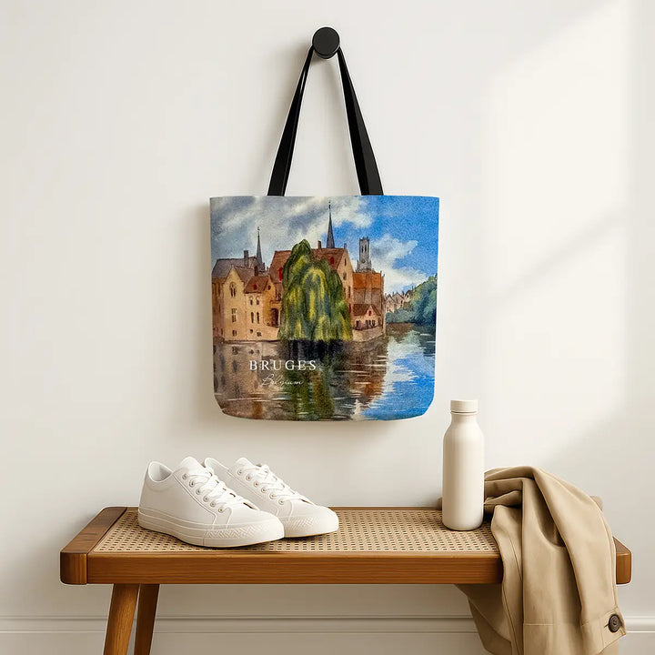 Tote bag with Bruges design hanging on a wall above a wooden bench with shoes and a bottle.