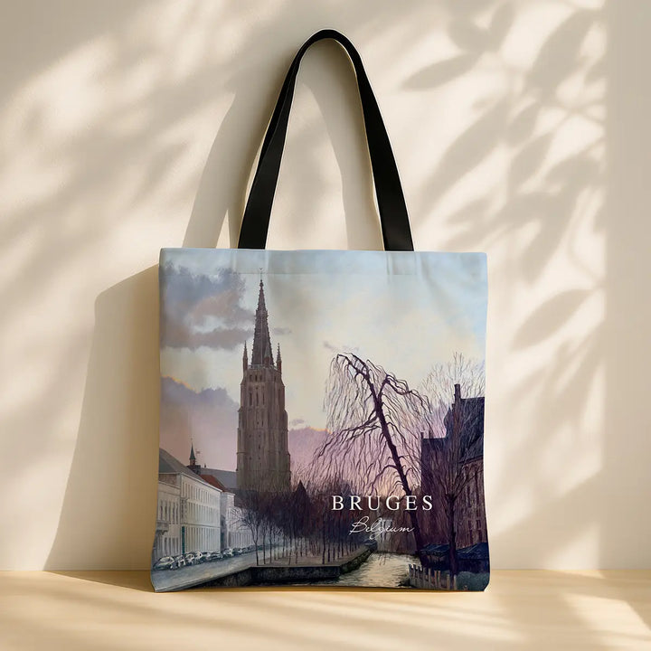 Tote bag with a scenic design of Bruges, featuring a tall tower and trees.